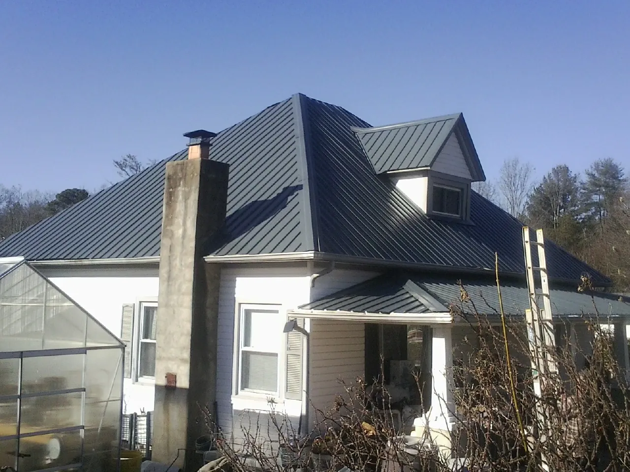 Dark blue standing seam metal roof on a white farmhouse with dormer — Slate & Tile Roof Repair by Roofing Brothers in South Milford