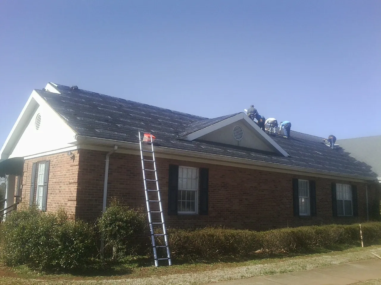 Crew tearing shingles off a brick ranch roof with a ladder set — Emergency Roof Repair work by our crew in South Milford