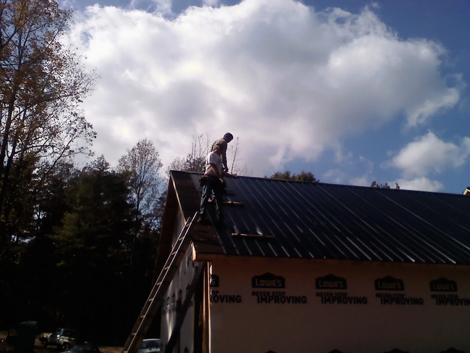 Roofer fastening dark metal panels high against a cloudy sky, from a Roof Inspection job in South Milford