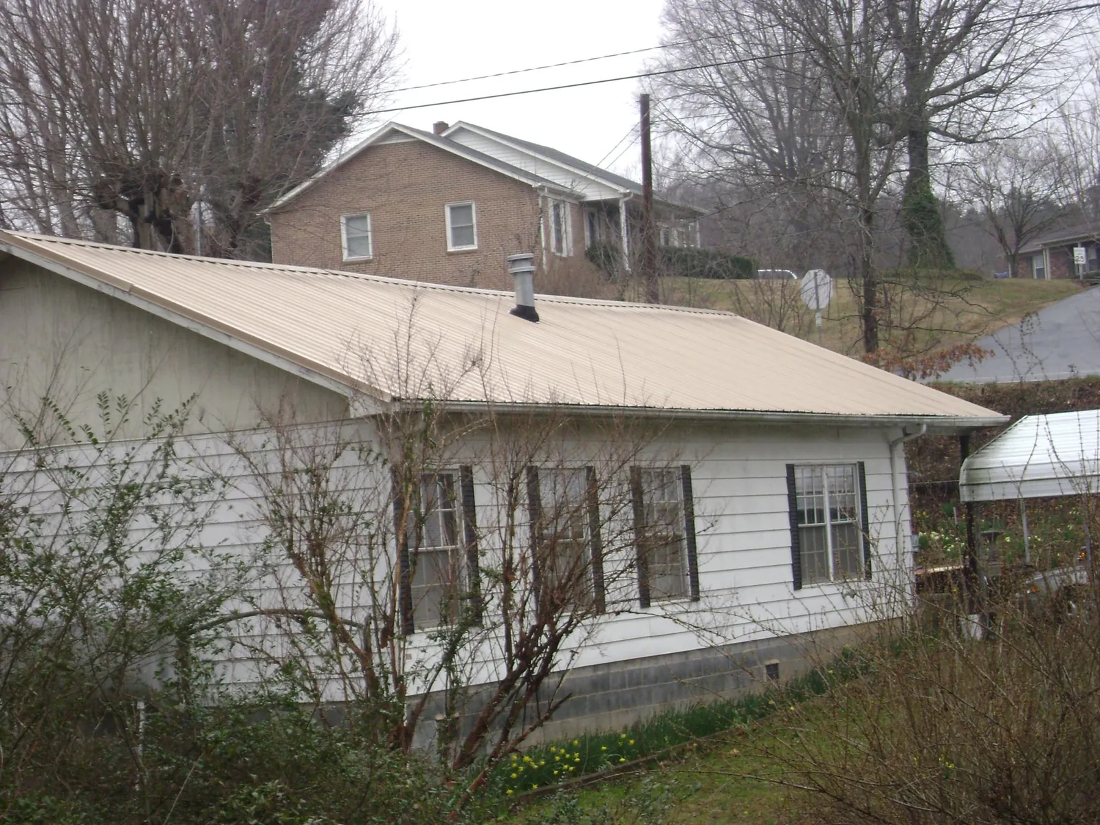 Tan metal roof on a white sided house set into a hillside — Commercial Roofing by Roofing Brothers in South Milford